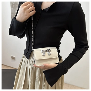 Détail d'un mini sac carré blanc crème avec un nœud en métal argenté et bandoulière chaîne