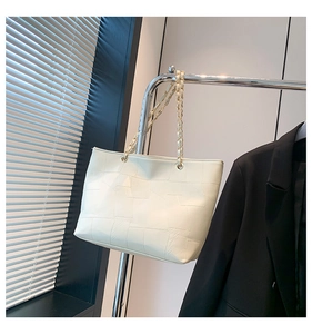 Detail view of cream tote bag featuring geometric patchwork and gold woven chain strap
