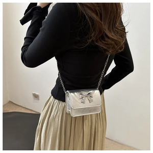 Petit sac argenté avec nœud métallique et bandoulière chaîne porté par un mannequin