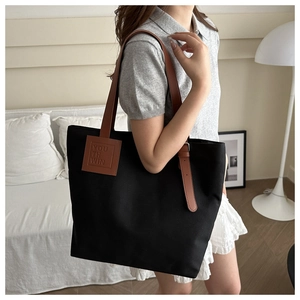 Detail of black canvas tote bag with brown leather straps shown in a lifestyle setting