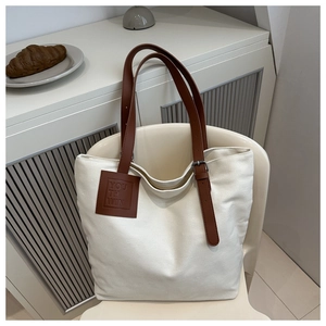Detail of canvas tote bag with brown leather adjustable straps and embossed logo tag