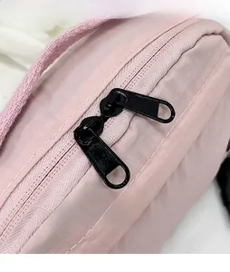 Detail of pink ripstop nylon crossbody bag featuring black dual metal zippers and strap buckle