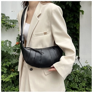 Detailansicht einer schwarzen Croissant-Tasche mit Falten auf einem beigen Blazer