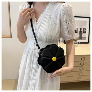 Fashionable black flower-shaped crossbody bag worn by a model in a warm home setting