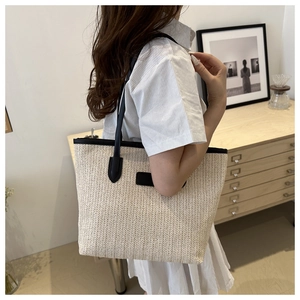 Détail d'un grand sac cabas en paille tressée avec bandoulière et écusson en cuir noir