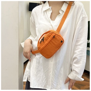 Detail of orange nylon crossbody bag featuring two zippered compartments and adjustable strap