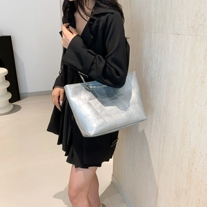 Minimalist silver metallic tote bag with chain strap shown on model in a modern room