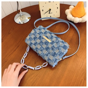 Détail d'un sac bandoulière en denim bleu clair à carreaux avec bords effilochés et chaîne