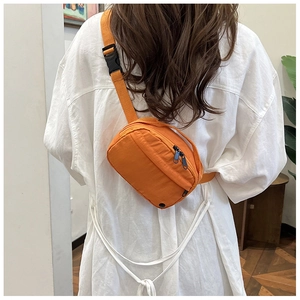 Rear view of model wearing an orange nylon crossbody bag with blue zipper detail