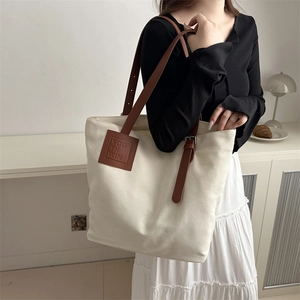 Minimalist off-white canvas tote bag with brown leather handles and brand patch logo