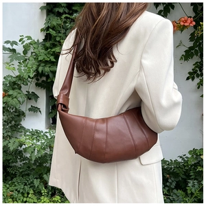 Detail der dunkelbraunen Leder-Croissant-Tasche mit Knotengurt am Modell im Freien