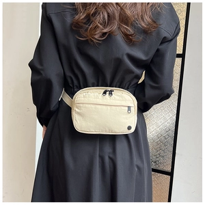 Minimalist beige nylon waist bag worn as a crossbody bag on a black dress backdrop