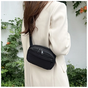 Close-up of a minimalist black crossbody bag worn by a model in a clean garden setting