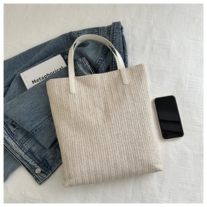 Flat lay of cream woven straw tote bag with white faux leather handles on a grid background