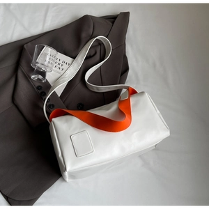 Chic white patent leather pillow bag with vibrant orange strap on a grey suit background