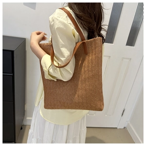 Close-up of woven straw tote bag featuring herringbone pattern and leather handles