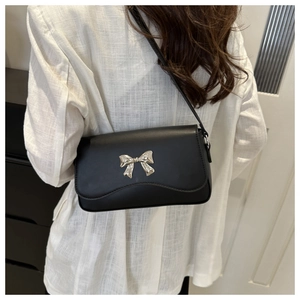 Close-up of a black crossbody bag with a silver butterfly metal buckle on a model