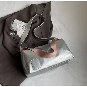 Detail of silver metallic cylindrical shoulder bag with pink contrast handles and leather tag