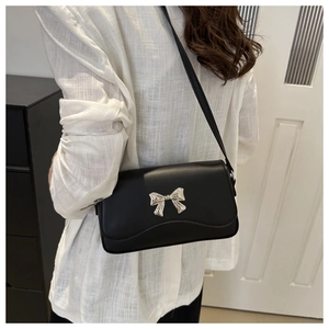 Detail of black glossy leather crossbody bag featuring a silver butterfly metal buckle