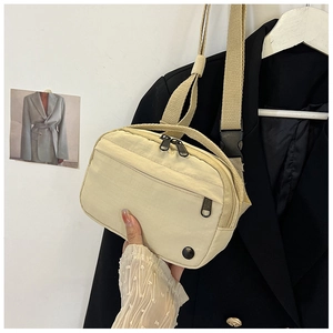 Detail of cream nylon crossbody bag with dual zippers and adjustable buckle strap