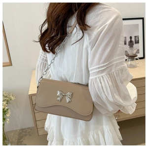 Detail of beige crossbody bag featuring a silver bow buckle and elegant metal chain strap