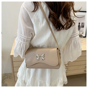 Detail of silver metal bow on beige small square crossbody bag with wavy flap