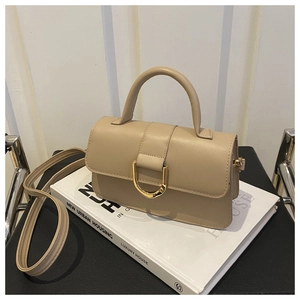 Détail du sac beige en similicuir avec boucle en D dorée sur un livre blanc