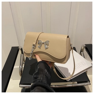 Detail of beige shoulder bag with wavy edge cover and silver metal bow decoration