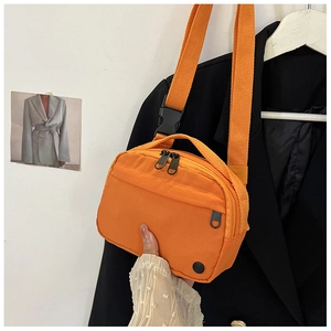 Detail of orange nylon crossbody bag with double zippers and black strap buckle