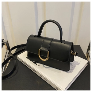 Détail du sac à main en cuir noir mat avec boucle en D dorée posé sur un livre blanc