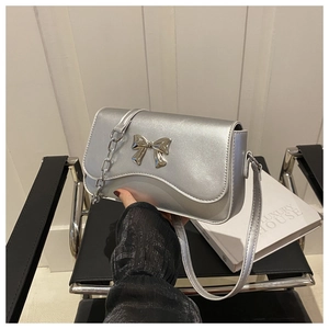 Detail of silver crossbody bag featuring a metallic bow ornament and link chain strap