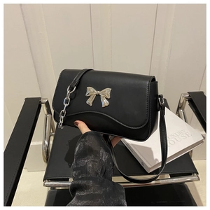 Close-up of black crossbody bag with silver bow hardware and metal chain strap detail