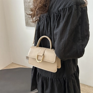 Sac bandoulière beige élégant avec boucle en D dorée présenté sur mannequin au décor épuré