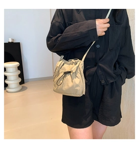 Détail d'un sac seau en nylon beige avec cordon de serrage porté par un mannequin