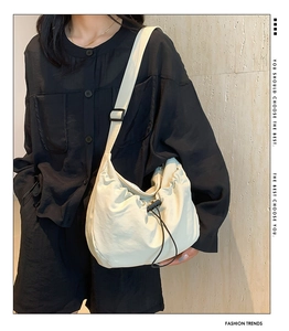 Detail of beige nylon crossbody dumpling bag with adjustable black strap on model