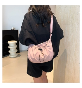 Detail of pink crossbody bag with adjustable strap and drawstring closure shown on model