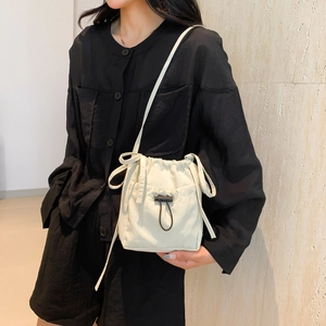 Sac seau minimaliste en nylon beige avec cordon de serrage porté par un mannequin