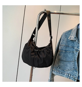 Detail of a black nylon crossbody cloud bag with drawstring pleats hanging by a jacket