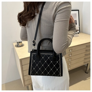 Close-up of black quilted shoulder bag with white embroidery and golden metal hardware