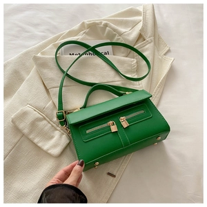 Dettaglio borsa in pelle verde con doppie cerniere dorate su un blazer beige elegante