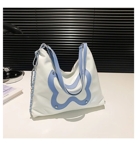 Detailed view of the white shoulder bag with blue butterfly patch and silver metal chain
