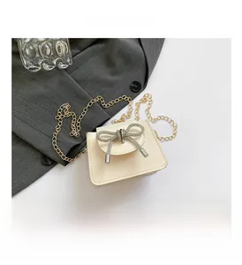 Detail of off-white mini crossbody bag with rhinestone bow and gold chain strap