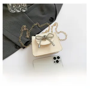 Close-up of cream crossbody bag with rhinestone bow detail and gold chain strap