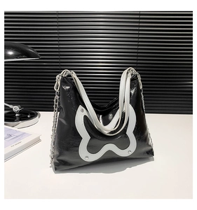 Detail of black leather shoulder bag featuring a white butterfly patch and silver metal studs
