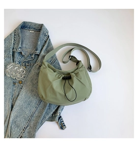 Close-up of sage green nylon crossbody bag with drawstring closure and pleat details