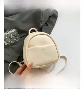 Vue détaillée d'un mini sac à dos crème avec poche avant et marquage lettre aimai