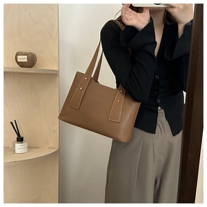 Detail einer braunen Leder-Tragetasche mit Goldnieten und Schultergurt am Modell