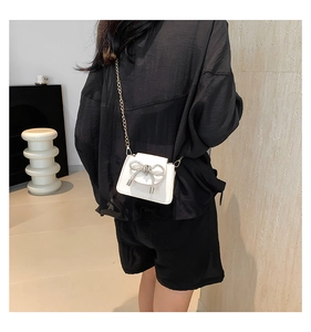 Detail of white mini crossbody bag with crystal bow buckle and gold chain strap on model