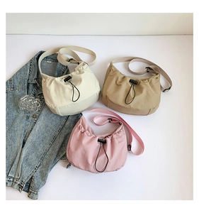 Detailed view of three nylon drawstring crossbody bags in cream, khaki, and soft pink colors