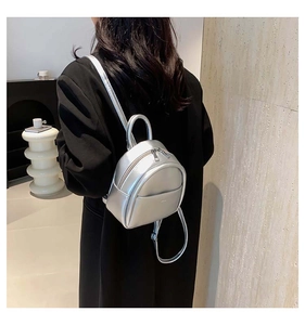 Mini sac à dos argenté métallisé porté avec un blazer noir dans un décor minimaliste